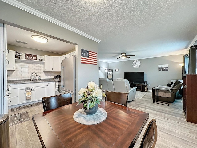 dining room featuring a textured ceiling, crown molding, sink, and light hardwood / wood-style flooring