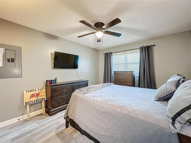 bedroom featuring ceiling fan, light wood-type flooring, a textured ceiling, and electric panel