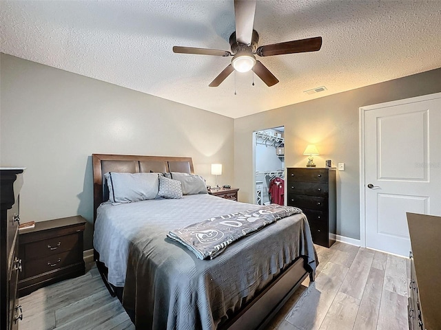 bedroom featuring a walk in closet, ceiling fan, light wood-type flooring, a textured ceiling, and a closet