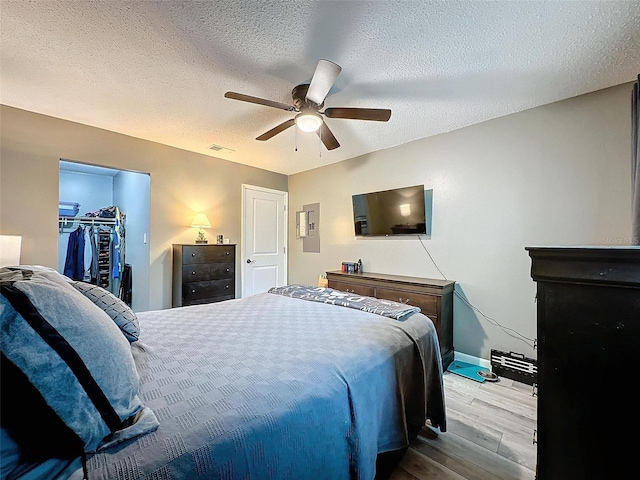 bedroom featuring a textured ceiling, ceiling fan, a spacious closet, light hardwood / wood-style flooring, and a closet