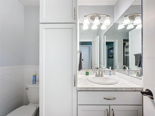 bathroom featuring vanity, toilet, and tile walls