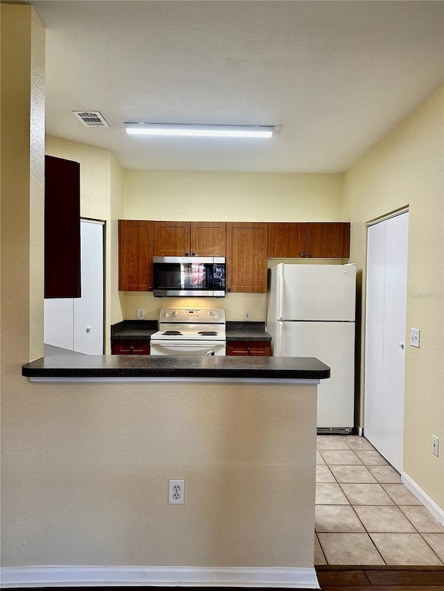 kitchen featuring white appliances, kitchen peninsula, and light tile patterned floors