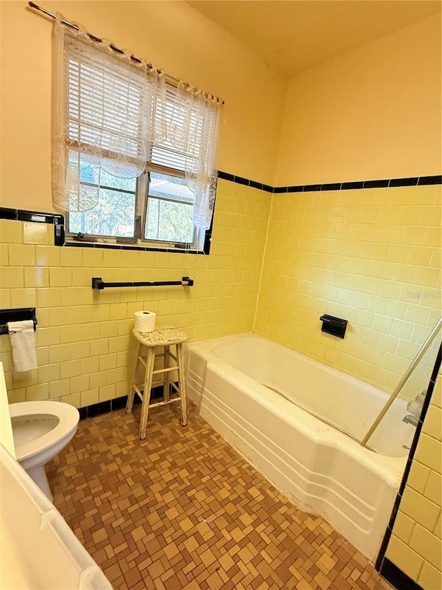 bathroom featuring a bathtub, toilet, and tile walls