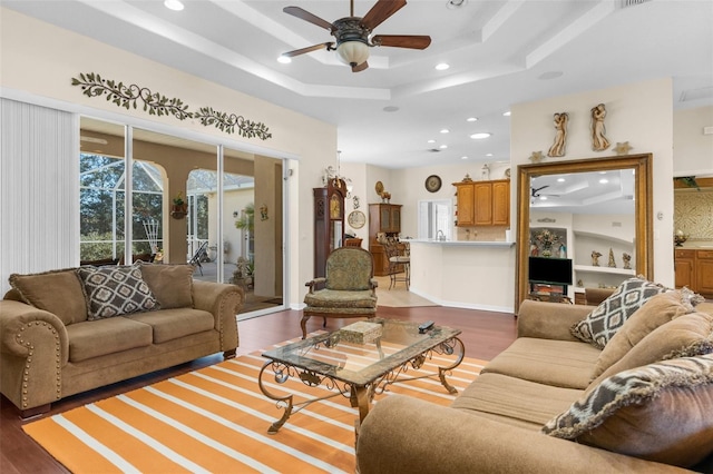 living room with a raised ceiling, ceiling fan, and dark hardwood / wood-style floors