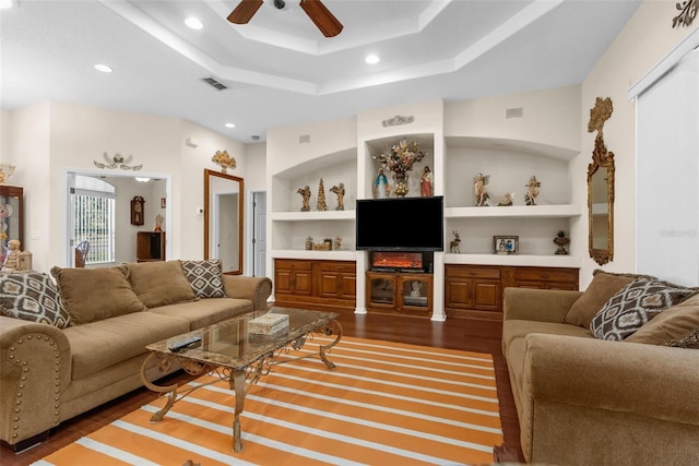 living room featuring a tray ceiling, ceiling fan, built in features, and dark wood-type flooring