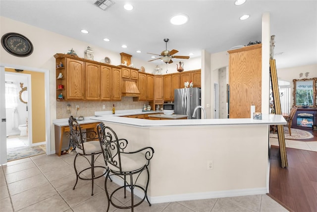 kitchen with a kitchen bar, stainless steel fridge, custom exhaust hood, ceiling fan, and light tile patterned floors