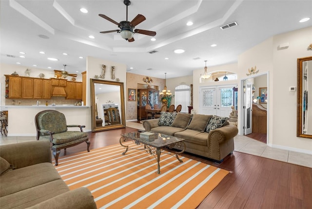 living room featuring a raised ceiling, french doors, ceiling fan with notable chandelier, and light wood-type flooring