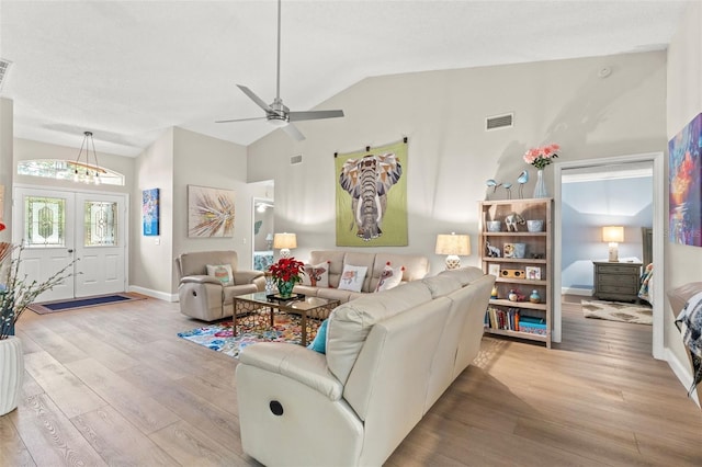 living room featuring ceiling fan with notable chandelier, french doors, light wood-type flooring, and vaulted ceiling