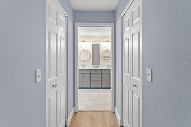 hallway featuring a textured ceiling, light wood-type flooring, and sink