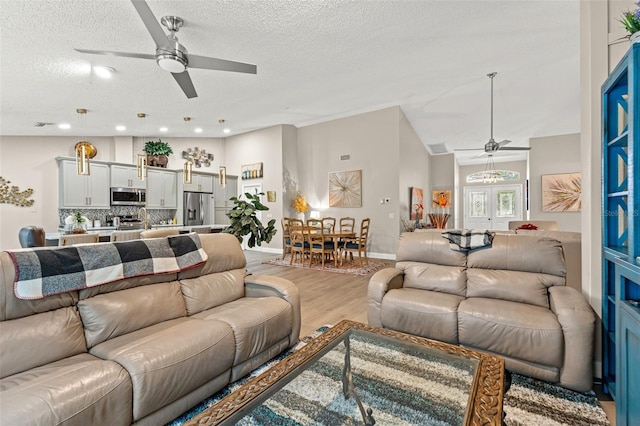 living room featuring vaulted ceiling, a textured ceiling, and light wood-type flooring