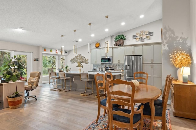 dining space featuring a textured ceiling, light hardwood / wood-style floors, and lofted ceiling