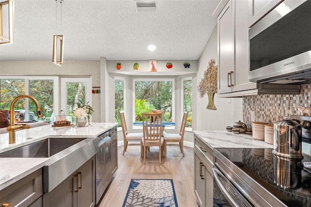 kitchen with decorative backsplash, light wood-type flooring, light stone counters, stainless steel appliances, and sink