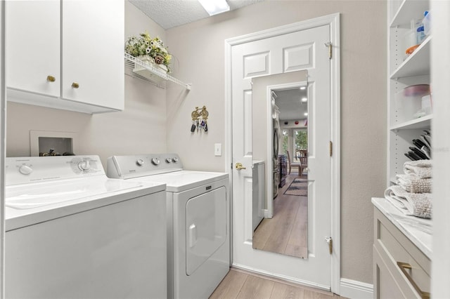 laundry area featuring washer and dryer, cabinets, a textured ceiling, and light hardwood / wood-style flooring