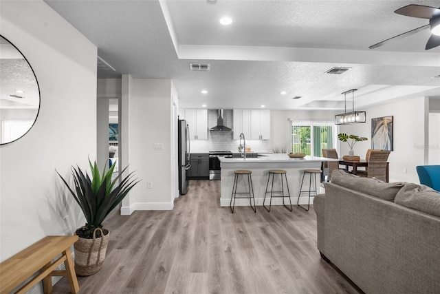 living room featuring a textured ceiling, a tray ceiling, ceiling fan, sink, and light hardwood / wood-style floors