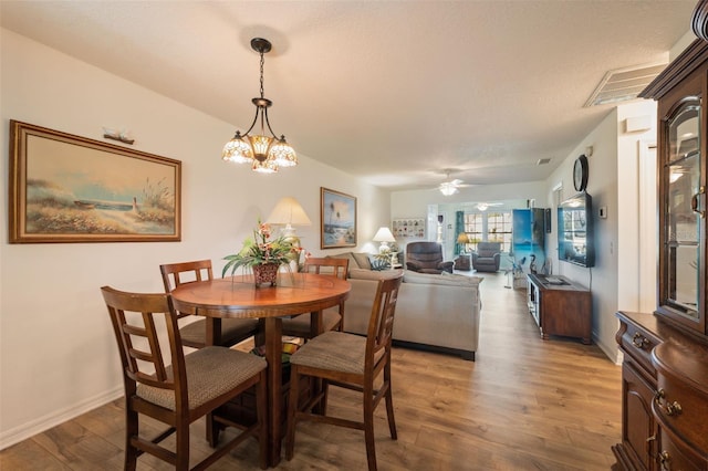 dining space with ceiling fan with notable chandelier, a textured ceiling, and dark hardwood / wood-style floors