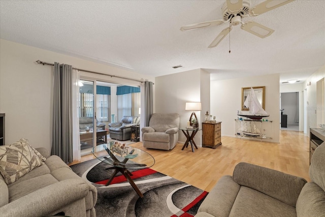 living room with a textured ceiling, ceiling fan, and wood-type flooring