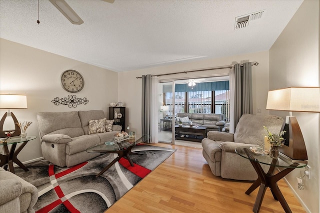 living room featuring ceiling fan, a textured ceiling, and wood-type flooring