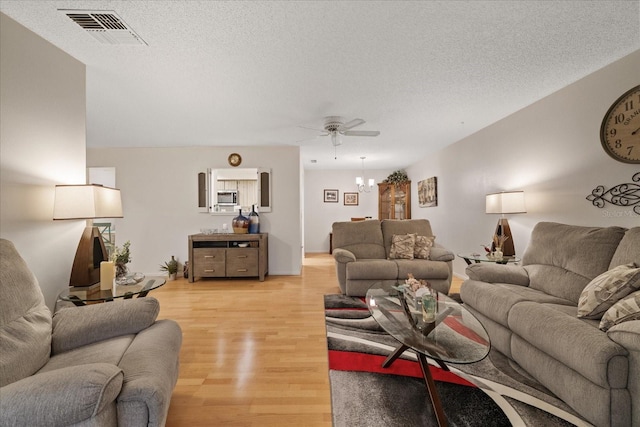 living room with ceiling fan with notable chandelier, a textured ceiling, and light hardwood / wood-style floors