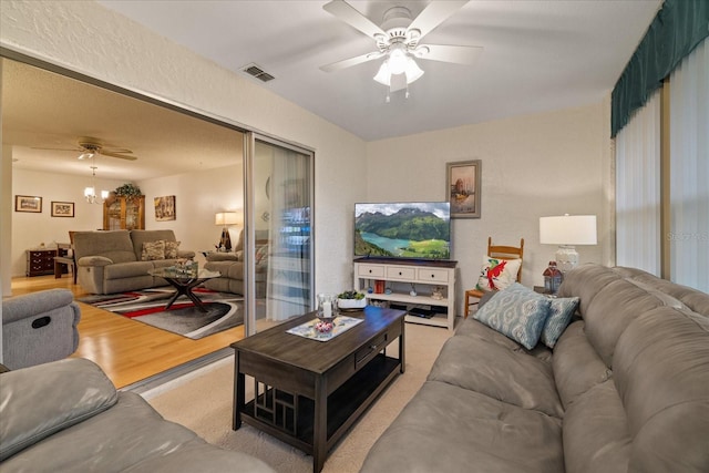 carpeted living room with ceiling fan with notable chandelier