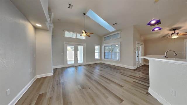 unfurnished living room with vaulted ceiling with skylight, ceiling fan, sink, and light hardwood / wood-style flooring