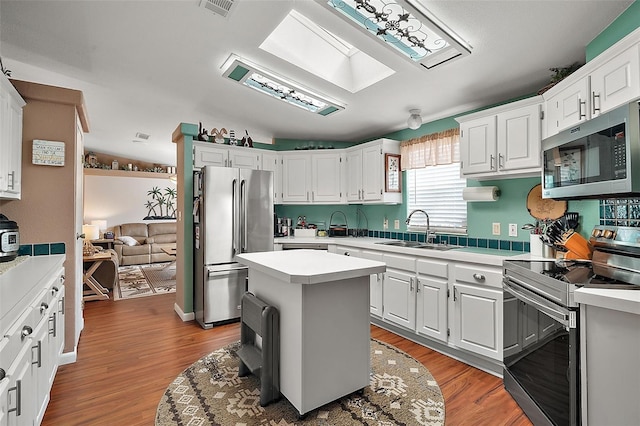 kitchen with white cabinetry, sink, wood-type flooring, a kitchen island, and appliances with stainless steel finishes