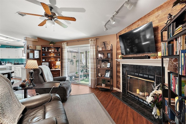 living room with lofted ceiling, a tile fireplace, rail lighting, dark hardwood / wood-style floors, and ceiling fan