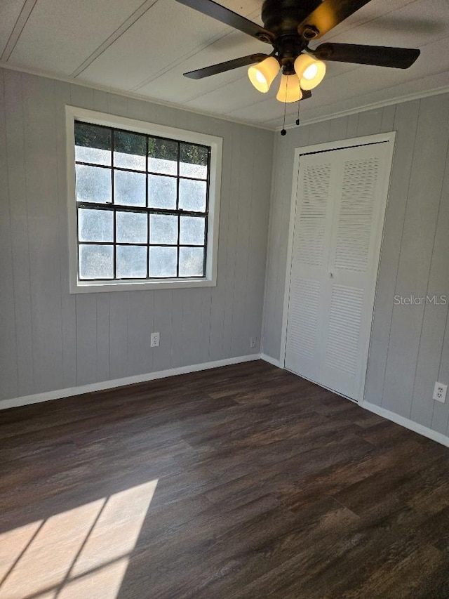 unfurnished bedroom featuring dark hardwood / wood-style flooring, a closet, ceiling fan, and wooden walls