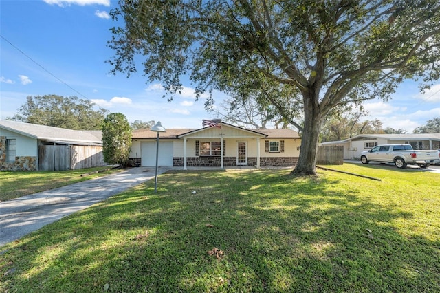 view of front of property featuring stone siding, fence, a garage, a front yard, and driveway