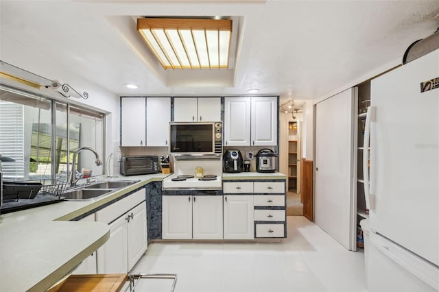 kitchen featuring white cabinets, stainless steel microwave, tasteful backsplash, a sink, and freestanding refrigerator