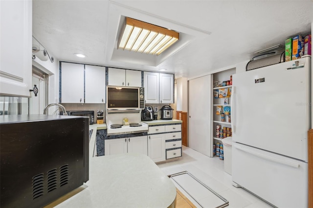 kitchen featuring freestanding refrigerator, light countertops, stovetop, and white cabinets