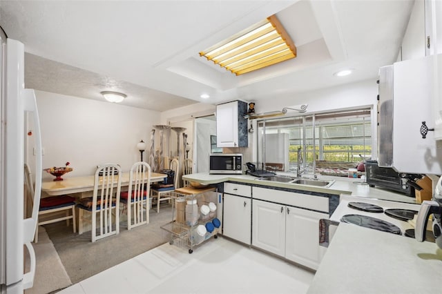 kitchen featuring stainless steel microwave, white cabinets, a sink, and a raised ceiling