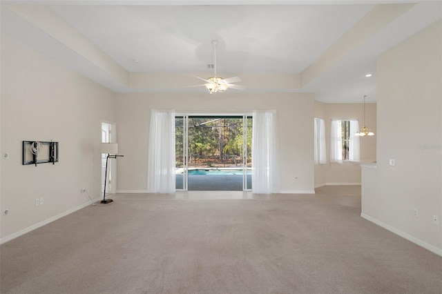 unfurnished living room featuring ceiling fan with notable chandelier, a tray ceiling, and light carpet