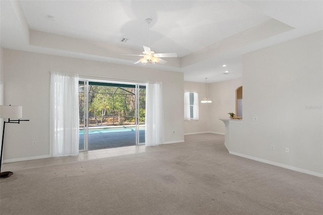 interior space featuring a raised ceiling, light carpet, ceiling fan, and a wealth of natural light