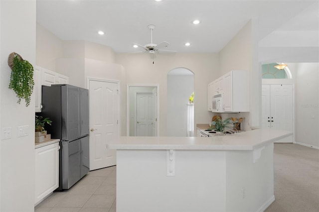 kitchen featuring kitchen peninsula, white cabinetry, a breakfast bar area, stainless steel refrigerator, and ceiling fan