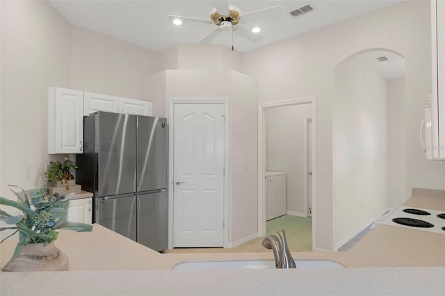 kitchen featuring washer and dryer, ceiling fan, stainless steel fridge, white cabinets, and sink