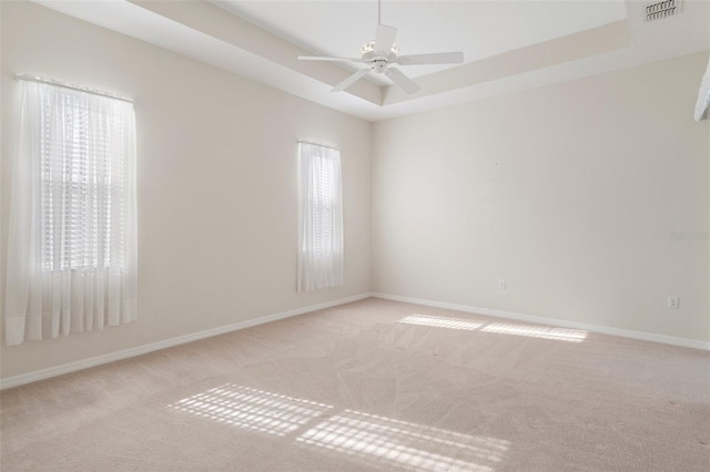 carpeted empty room with ceiling fan and a tray ceiling