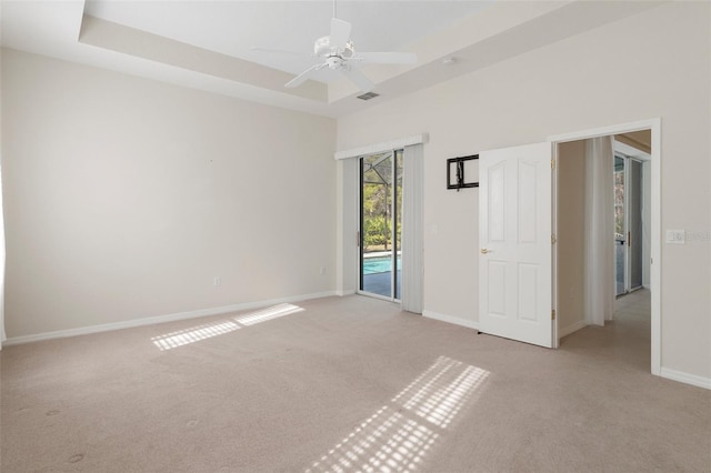 spare room featuring ceiling fan, a tray ceiling, and light carpet