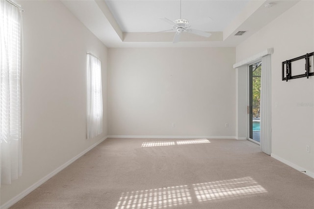 empty room with a raised ceiling, light colored carpet, and ceiling fan