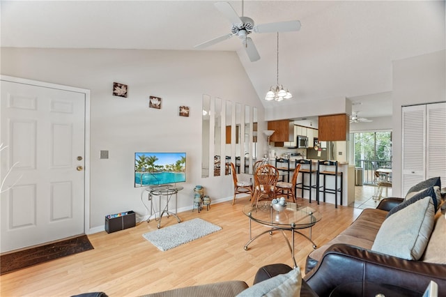 living room with ceiling fan with notable chandelier, high vaulted ceiling, and light hardwood / wood-style flooring