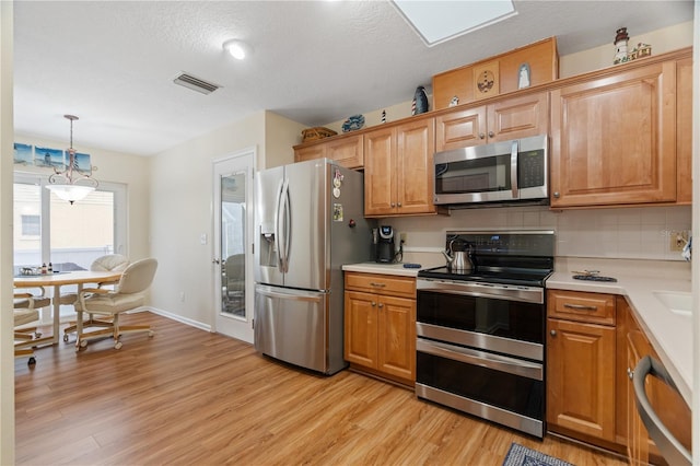 kitchen with tasteful backsplash, pendant lighting, light wood-type flooring, and appliances with stainless steel finishes