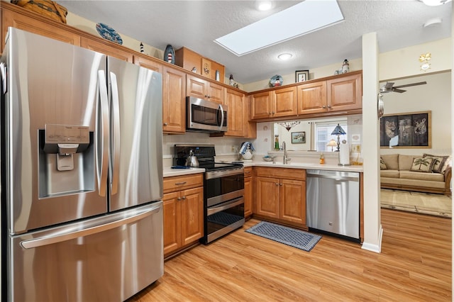 kitchen with sink, a skylight, ceiling fan, light wood-type flooring, and stainless steel appliances