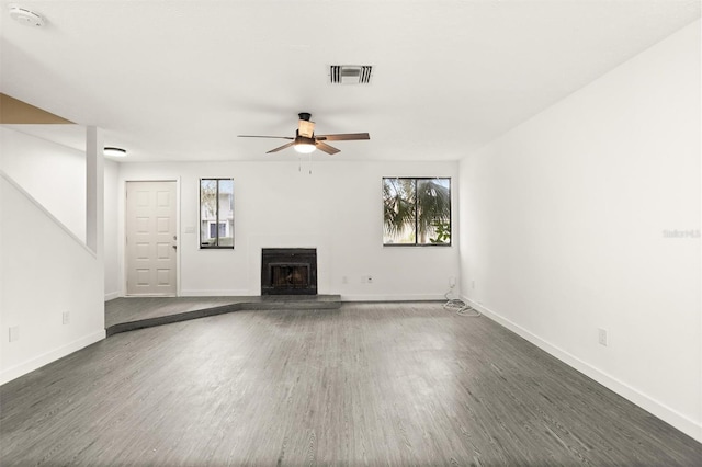 unfurnished living room with a wealth of natural light, dark wood-type flooring, and ceiling fan