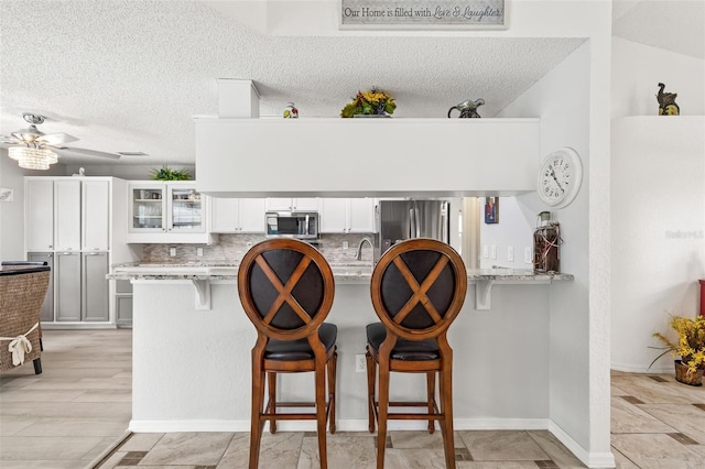 kitchen with white cabinets, stainless steel appliances, light stone countertops, and kitchen peninsula