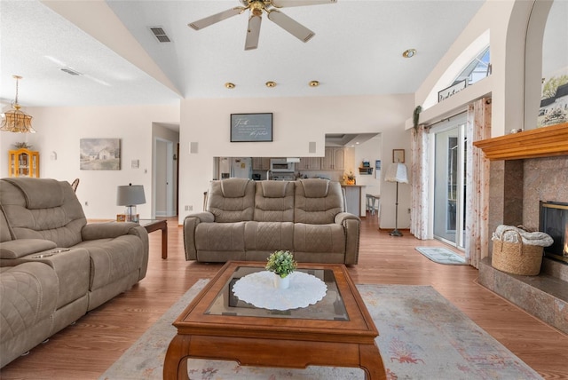 living room featuring ceiling fan, light wood-type flooring, lofted ceiling, and a fireplace