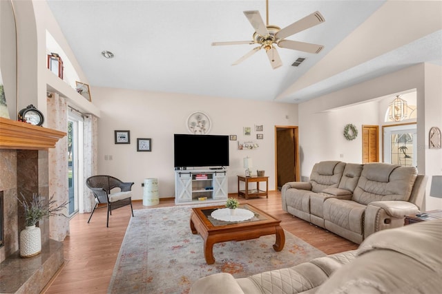 living room with light hardwood / wood-style floors, a tile fireplace, ceiling fan, and vaulted ceiling