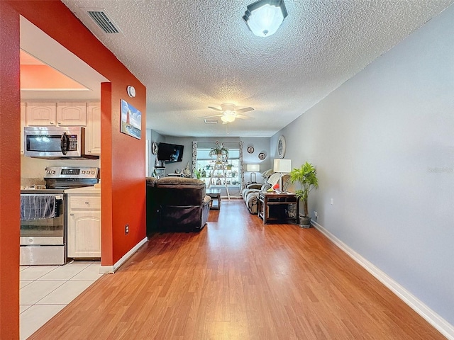 living room with ceiling fan, light wood-type flooring, and a textured ceiling