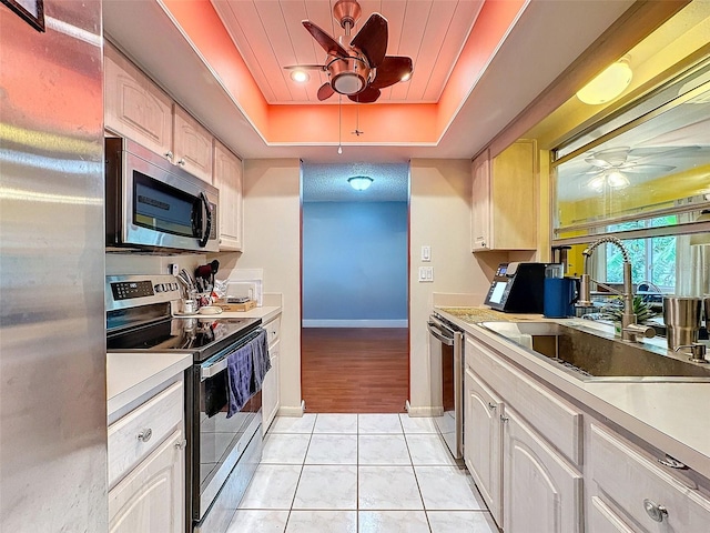 kitchen with sink, light tile patterned floors, a tray ceiling, white cabinets, and appliances with stainless steel finishes