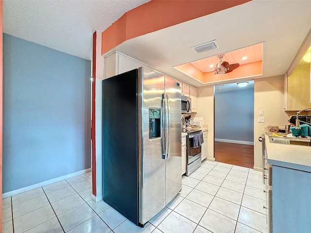 kitchen with appliances with stainless steel finishes, a raised ceiling, ceiling fan, sink, and light tile patterned floors