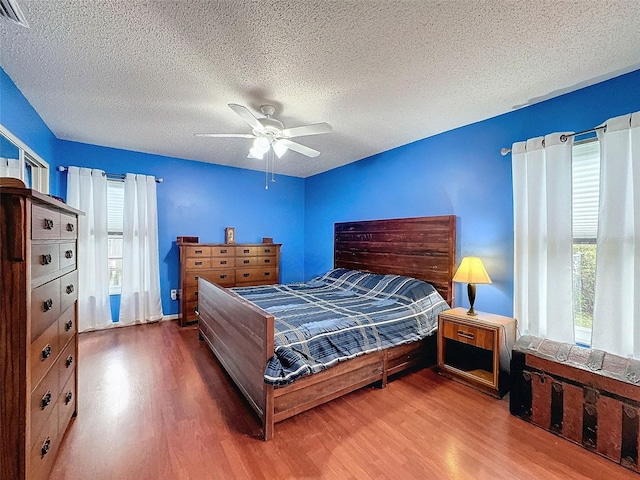 bedroom with ceiling fan, wood-type flooring, and a textured ceiling