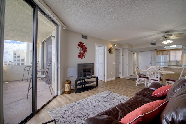 living room with light hardwood / wood-style floors, a textured ceiling, and ceiling fan